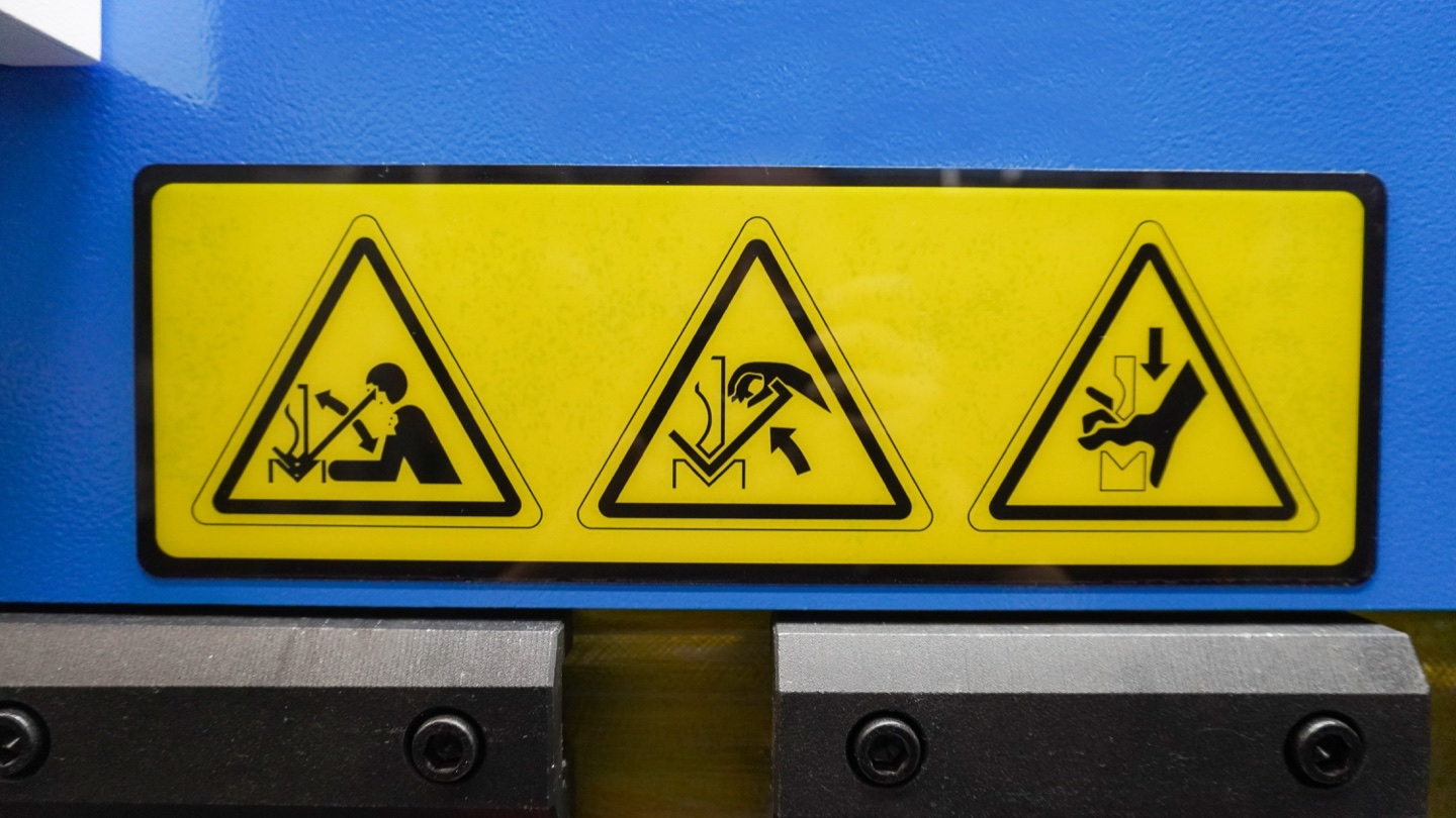 Crushing and pinch-point warning symbols at the press brake tooling area.